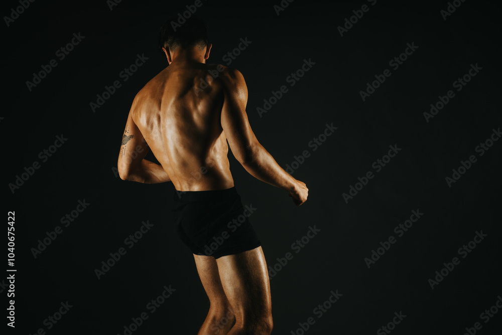 Fit man displaying his strong back muscles in a low light studio environment, showcasing fitness and strength. Fit man displaying his strong back muscles in a low light studio environment, showcasing fitness and strength.