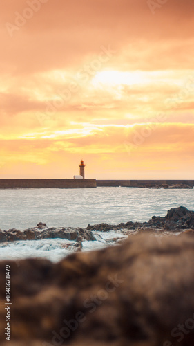 Porto lighthouse silhouette against golden sunset sky with dramatic waves and rocky shore