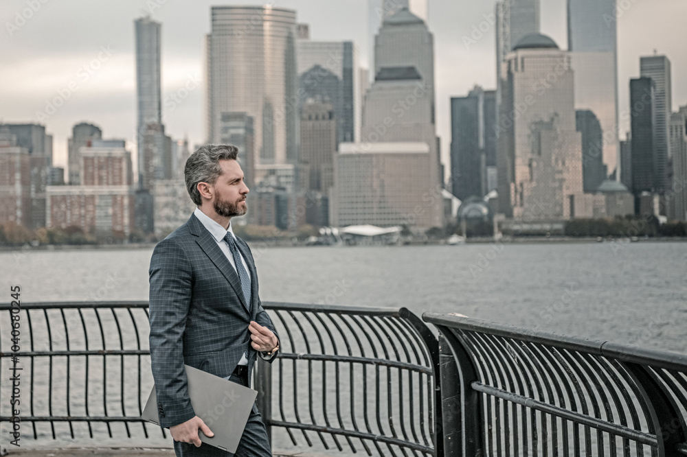 Business man in suit holding laptop on urban street in NYC. Successful business man outdoor. Middle aged business man standing outside office using laptop. Street portrait of mature businessman. Business man in suit holding laptop on urban street in NYC. Successful business man outdoor. Middle aged business man standing outside office using laptop. Street portrait of mature businessman.