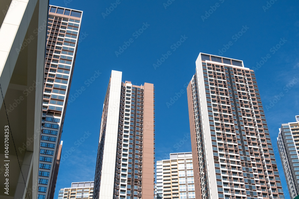 A low-angle view of modern high-rise residential buildings against a clear blue sky. Apartment complex with concrete facades, creating a sleek, urban aesthetic. Concept of contemporary city life A low-angle view of modern high-rise residential buildings against a clear blue sky. Apartment complex with concrete facades, creating a sleek, urban aesthetic. Concept of contemporary city life