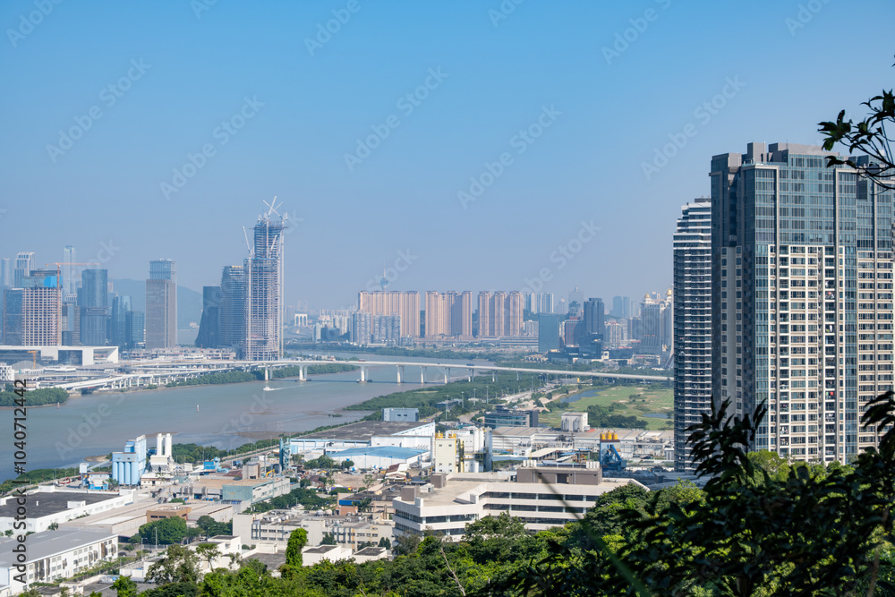 Obraz premium Panoramic view of the dynamic cityscape of Macau and Hengqin Island, featuring modern skyscrapers and towering buildings along the waterfront, showcasing the infrastructure and urban development.