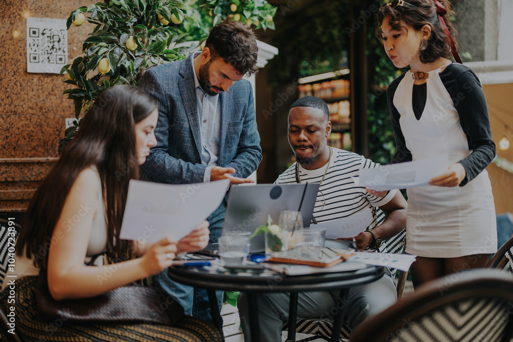 Multiracial group of business professionals collaborating and strategizing in a modern coffee bar. They are engaged in discussion, sharing ideas and reviewing documents for a project.