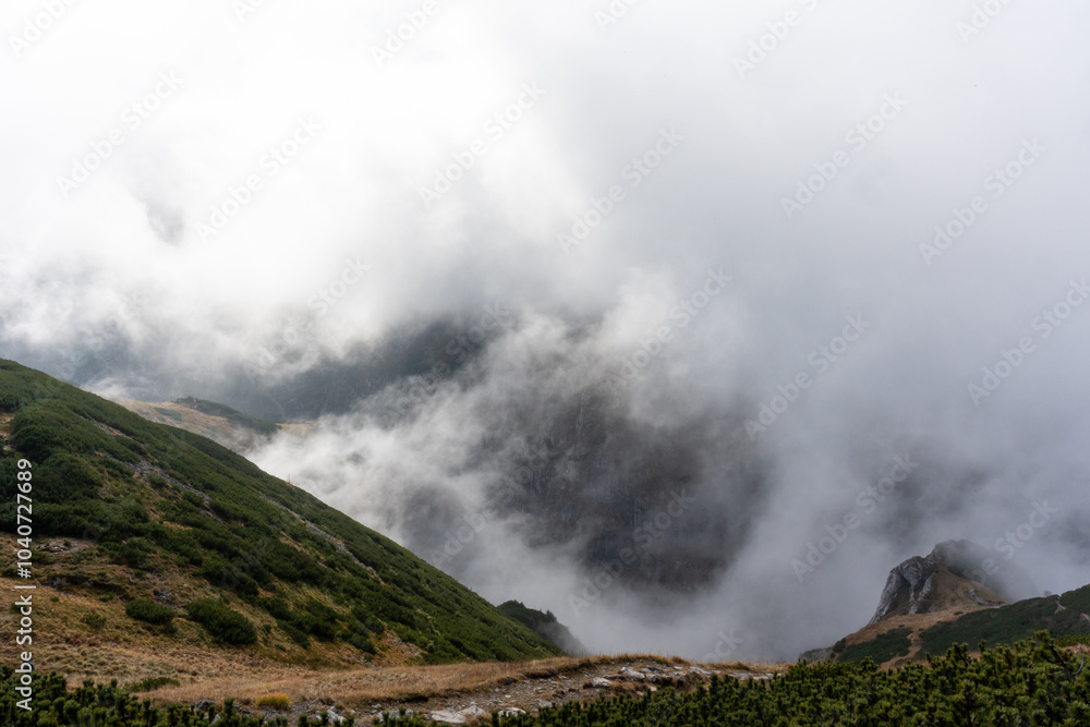 Clouds of mist rolling over green mountain slopes with a rocky outcrop partially visible. Concept of dramatic landscape, nature is beauty, and hiking through foggy wilderness. High quality photo Clouds of mist rolling over green mountain slopes with a rocky outcrop partially visible. Concept of dramatic landscape, nature is beauty, and hiking through foggy wilderness. High quality photo