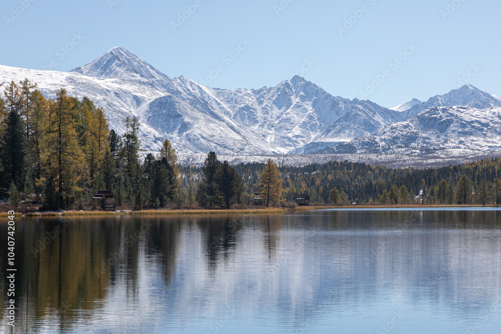 Panoramic landscape of a mountain lake in a northern nature: snowy mountain peaks, dense coniferous forest. The season is golden autumn, September: yellow and red red grass, golden foliage. Panoramic landscape of a mountain lake in a northern nature: snowy mountain peaks, dense coniferous forest. The season is golden autumn, September: yellow and red red grass, golden foliage.