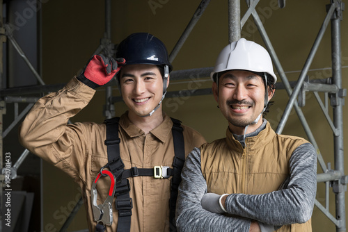 鳶職や屋外の安全帯ハーネスをつけた作業のガテン系作業員二人の 仲良しカメラ目線笑顔　腕組み photo