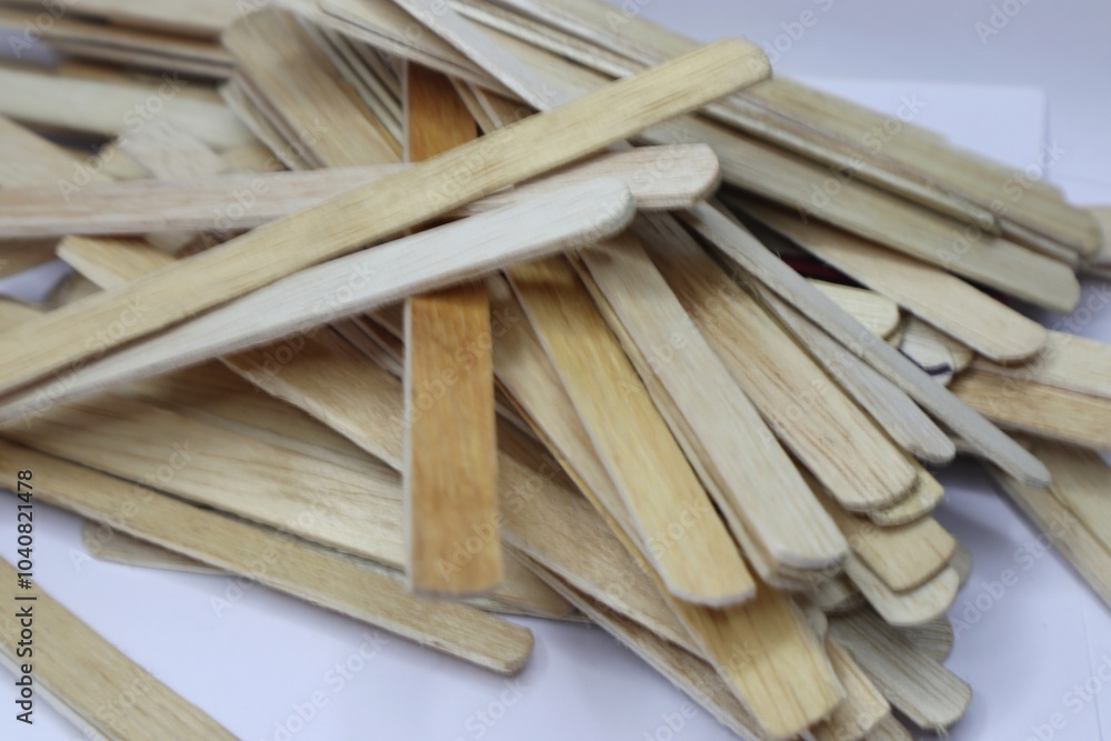A pile of wooden popsicle sticks. The sticks are of various lengths and have a natural, light brown color. A pile of wooden popsicle sticks. The sticks are of various lengths and have a natural, light brown color.