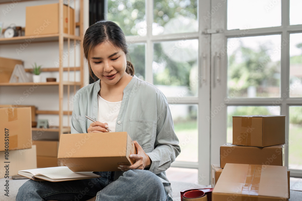Young Woman Small Business Owner Preparing Online Orders in Home Office with Cardboard Boxes and Laptop Young Woman Small Business Owner Preparing Online Orders in Home Office with Cardboard Boxes and Laptop