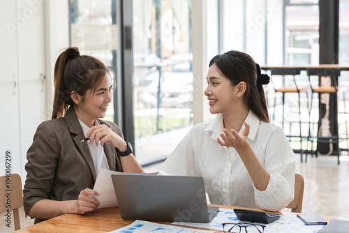 Young businesswoman and colleague collaboration in a modern office environment, discussing ideas and working together on a project with a laptop, documents, and charts, fostering teamwork and