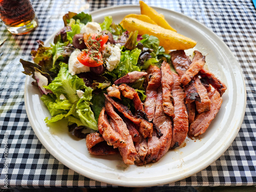 A plate of lamb flank steak and salad on a checkered table. The salad is topped with cheese and tomatoes