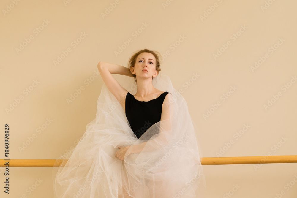Fototapeta premium A ballet dancer poses with tulle fabric in a serene studio setting, embodying grace and artistry.