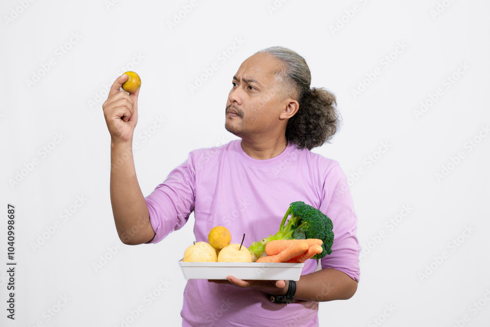 An Indonesian curly long-haired man holding a orange while carrying a tray of fruit and vegetables, healthy life concept
An Indonesian curly long-haired man holding a orange while carrying a tray of fruit and vegetables, healthy life concept
