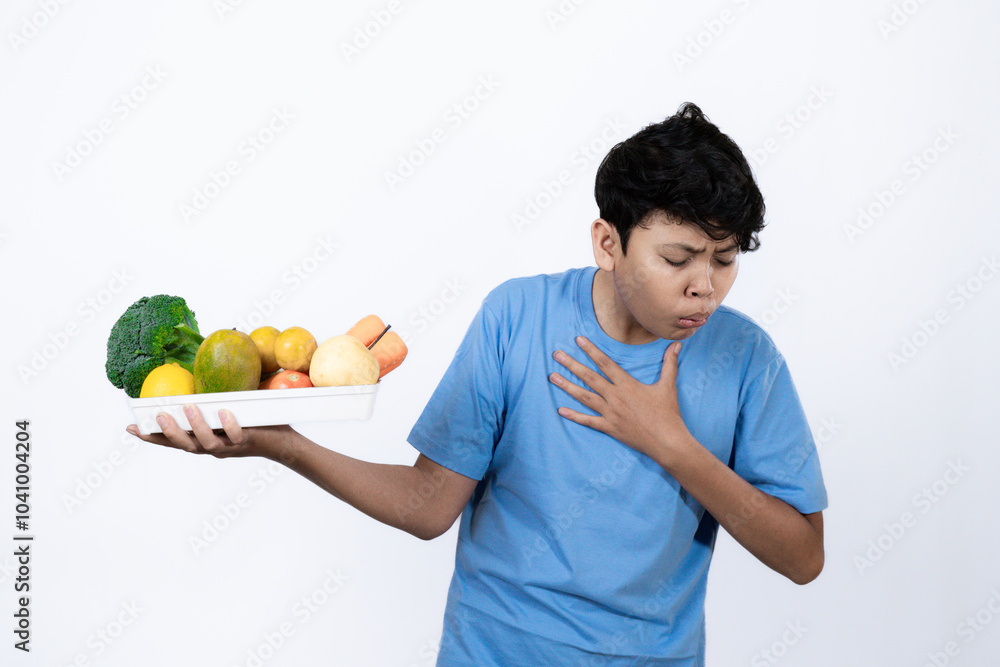 Young excited Indonesian man standing carrying tray of healthy vegetables and fruits with his hand pointing, healthy lifestyle concept, healthy food campaign, isolated on white background. Young excited Indonesian man standing carrying tray of healthy vegetables and fruits with his hand pointing, healthy lifestyle concept, healthy food campaign, isolated on white background.