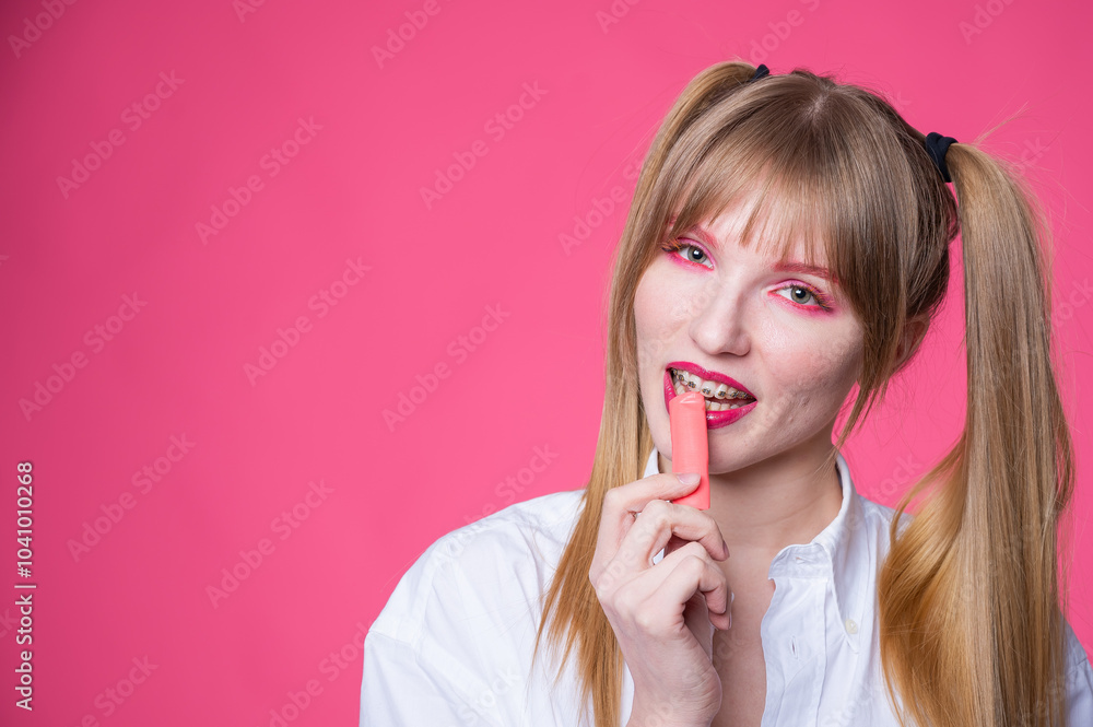 Portrait of a young woman with braces and bright makeup chewing gum on a pink background. Portrait of a young woman with braces and bright makeup chewing gum on a pink background.