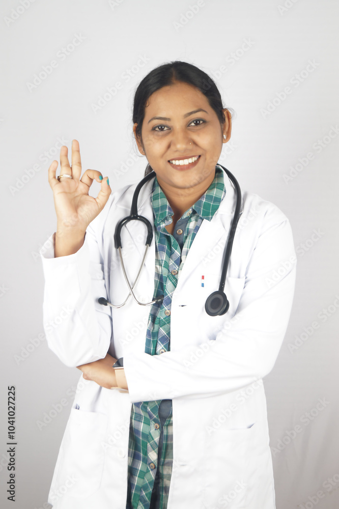 young woman doctor in white coat making ok sign with onehand, standing on white background, smiling at camera. Medical help, health care recommendation, good news gesture fold her hand young woman doctor in white coat making ok sign with onehand, standing on white background, smiling at camera. Medical help, health care recommendation, good news gesture fold her hand
