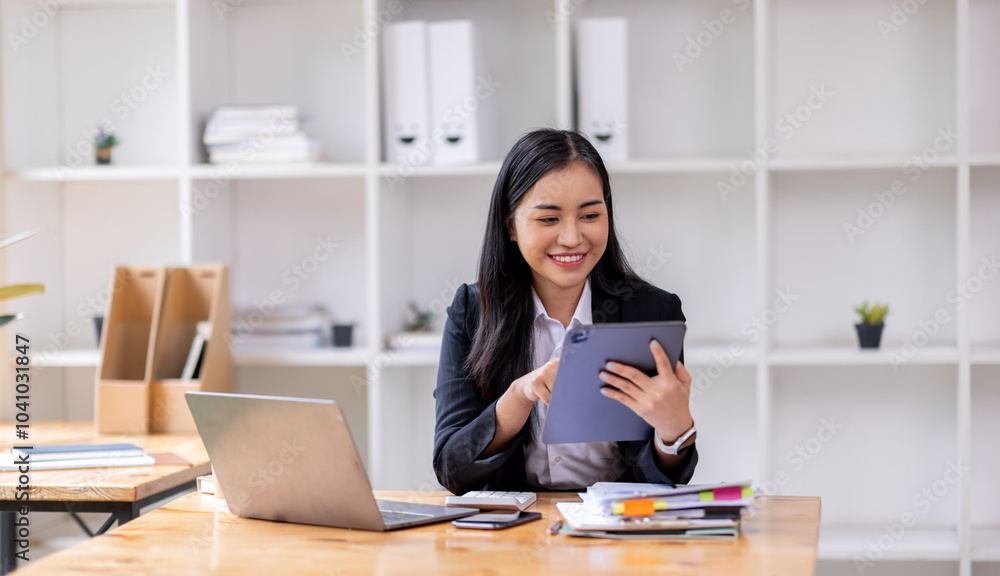 Female business person using digital tablet and laptop or remote working at office, looking at digital tablet watching webinar, learning training, studying online seminar or video calling.
