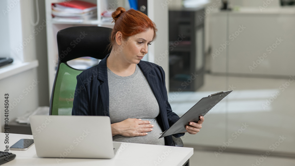 Pregnant woman reading documents on a paper tablet in the office. Pregnant woman reading documents on a paper tablet in the office.