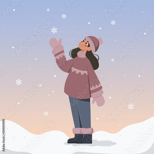 A carefree young woman in warm and comfortable winter clothes catches falling snowflakes.
