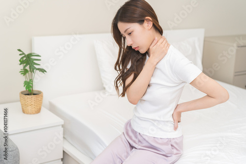 Pain body muscles stiff problem, asian young woman painful with back, neck ache from work hand holding massaging rubbing shoulder hurt, sore sitting on bed in room at home. Health care and medicine. photo