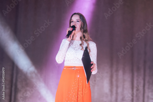 A girl hosting a concert with a microphone on stage in the spotlight. photo