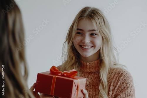 A young woman in a cozy sweater smiles joyfully as she receives a red gift box tied with a ribbon.