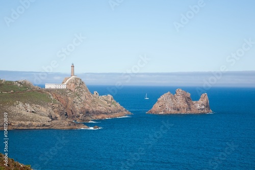 Cape Vilan lighthouse and rocky coastline with sailboat photo