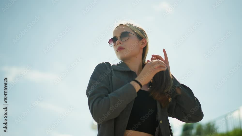 Lady wearing black crop top under grey shirt gently holds her hair while looking away, she stands outdoors on a sunny day, her hair fluttering slightly in the wind Lady wearing black crop top under grey shirt gently holds her hair while looking away, she stands outdoors on a sunny day, her hair fluttering slightly in the wind