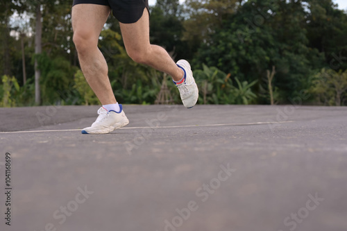 Low angle shot sportsman legs in sport shoes jogging along a paved road. Fitness and active lifestyle