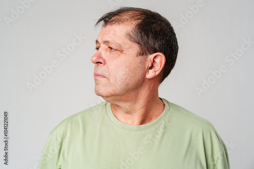 Man in a green shirt gazing thoughtfully to the side in a minimalist setting