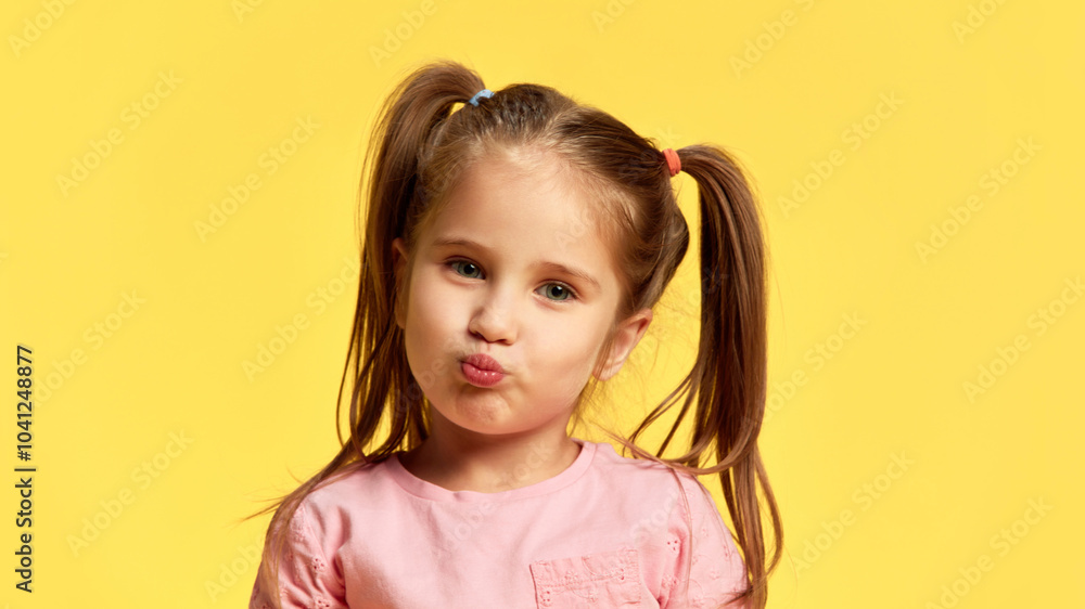 Little girl puckers her lips, giving cute kiss or duck face look. Her expression innocent and playful against sunny yellow background. Concept of facial-expressions, positive and negative emotions. Ad Little girl puckers her lips, giving cute kiss or duck face look. Her expression innocent and playful against sunny yellow background. Concept of facial-expressions, positive and negative emotions. Ad
