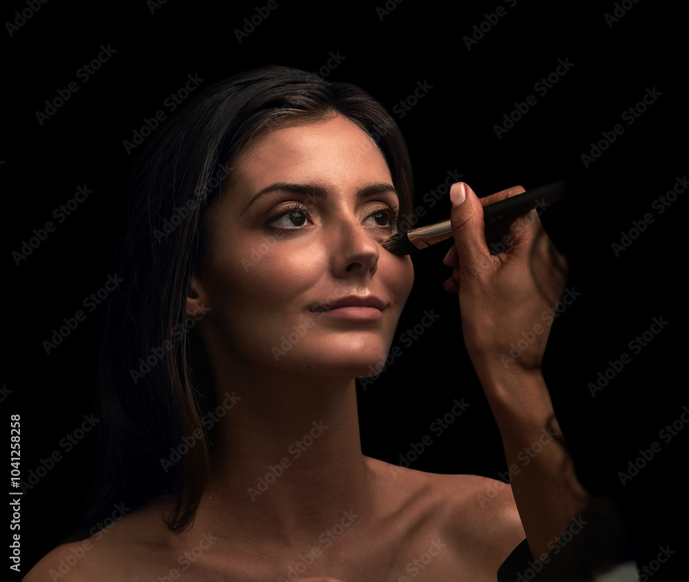 Obraz premium Woman, hand and apply makeup in studio with brush, beauty cosmetics and facial glow of transformation. Girl, tools and artist for foundation, skincare treatment and aesthetic style on dark background