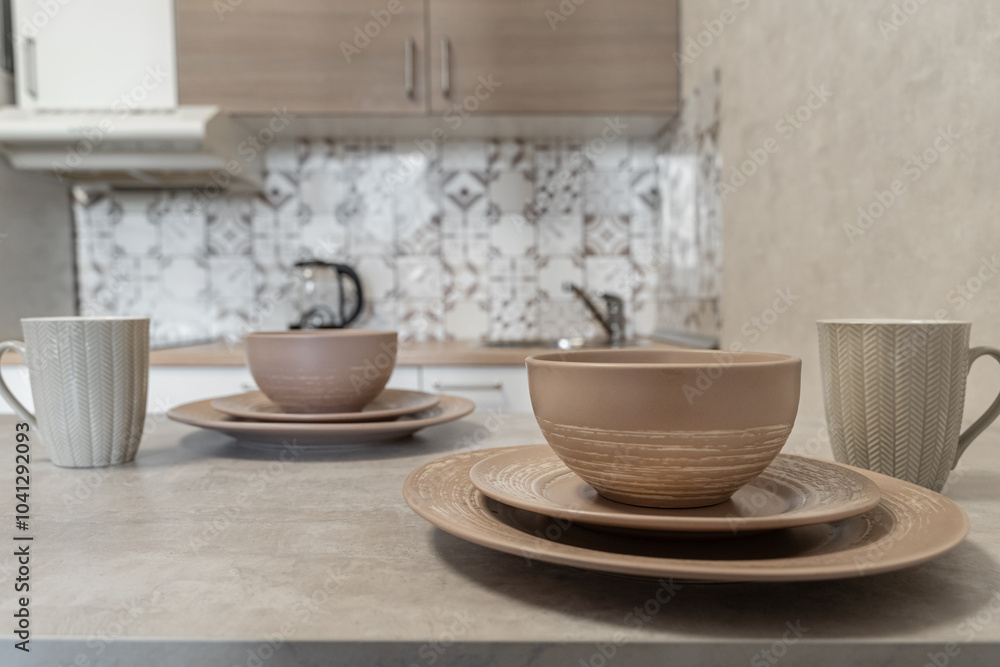 design of modern beige kitchen. brown dishes on kitchen table. Plates of different sizes and ceramic mugs. Setting table for breakfast, lunch or dinner. cozy evening at home. Breakfast for two. design of modern beige kitchen. brown dishes on kitchen table. Plates of different sizes and ceramic mugs. Setting table for breakfast, lunch or dinner. cozy evening at home. Breakfast for two.