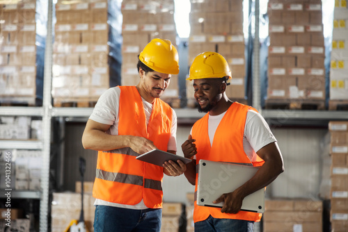 Fotografi Interracial foreign industry employees standing at warehouse with tablet and laptop and planning logistic