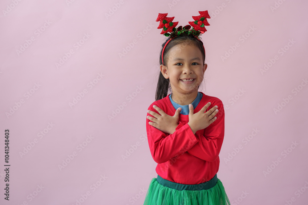 Adorable little Asian girl with Christmas tree headband, antlers showing various poses, standing, smiling, laughing, having fun in various poses, pink background. Holiday concept annual festival. Adorable little Asian girl with Christmas tree headband, antlers showing various poses, standing, smiling, laughing, having fun in various poses, pink background. Holiday concept annual festival.