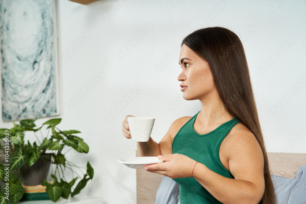 A petite brunette woman relaxes in her cozy home, savoring tea while surrounded by plants and tranquility. A petite brunette woman relaxes in her cozy home, savoring tea while surrounded by plants and tranquility.