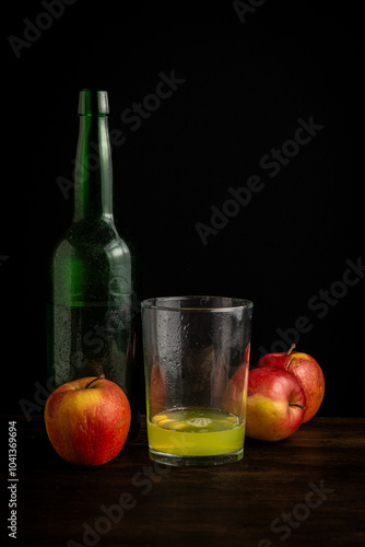 View of bottle and glass with natural cider on dark table with apples, black background vertically with copy space