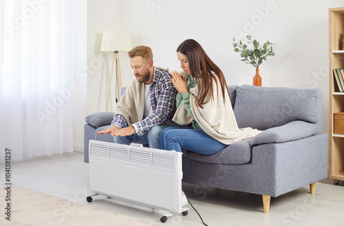 Family couple near heater on couch at home freezing in cool flat in blanket shivering tremble with cold, unhappy people feel bad suffer of heating system problems, feeling unwell, freezing temperature