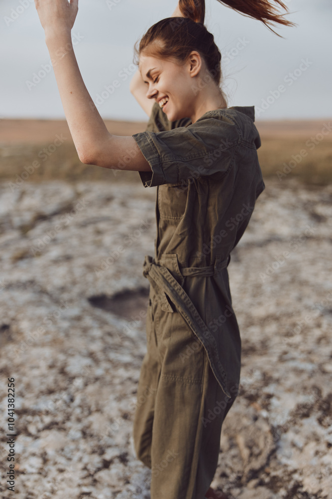 Woman in olive green jumpsuit standing on rocky field with hands raised in air for fashion and beauty magazine cover Woman in olive green jumpsuit standing on rocky field with hands raised in air for fashion and beauty magazine cover