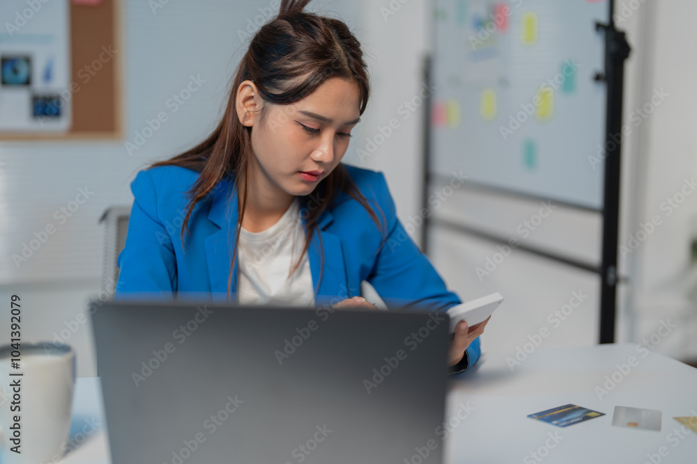 Businesswoman concentrating while using calculator and working on laptop to analyze financial data and make investment decisions Businesswoman concentrating while using calculator and working on laptop to analyze financial data and make investment decisions