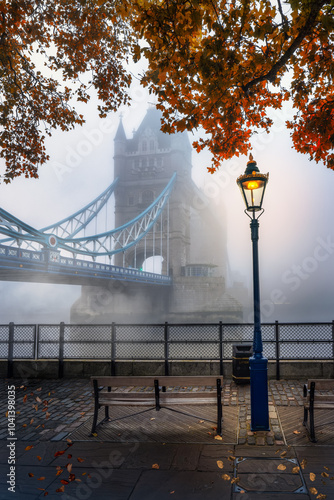 Moody autumn view of the Tower Bridge in London with fog, England, with golden foliage