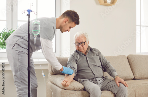 Cuadro en lienzo Young friendly nurse help gray-haired sick senior elderly man in receiving IV drip infusion and vitamin injection therapy sitting on sofa at home or in medical clinic