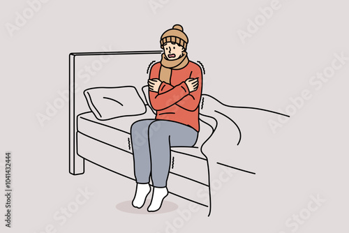 Freezing man is shaking sitting on bed and feeling chills and cold, dressed in hat and scarf. Freezing guy suffers due to lack of central heating system and poor immunity, located in bedroom