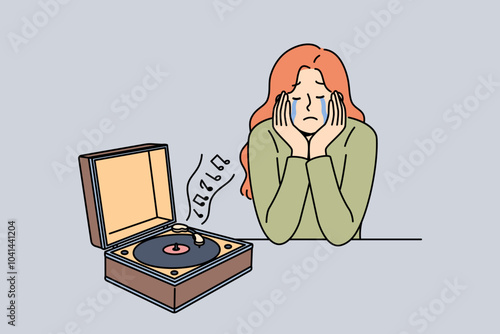 Woman cries listening to music on vinyl player, due to nostalgia and memories of happy past. Girl experiences nostalgia after launching retro device with audio album from last century