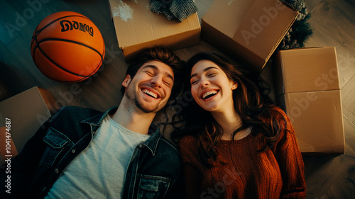 A happy couple lying on the floor in their new apartment, laughing and enjoying each other's company. They have boxes around them with basketballs nearby. Top view. Shot with a Nikon D850 DSLR camera  photo