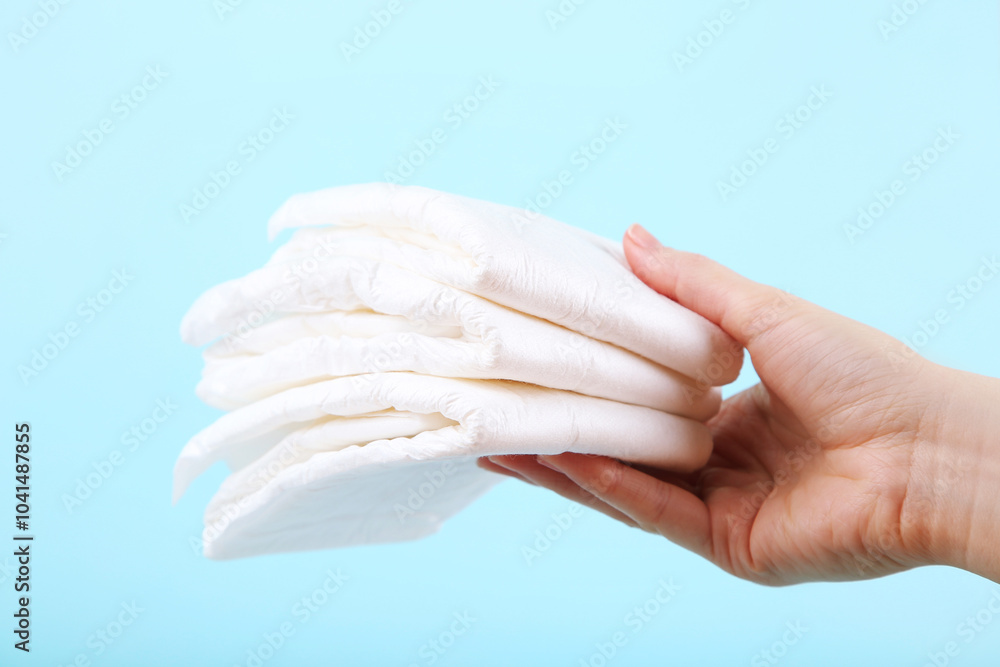 Baby diapers with female hand on blue background
