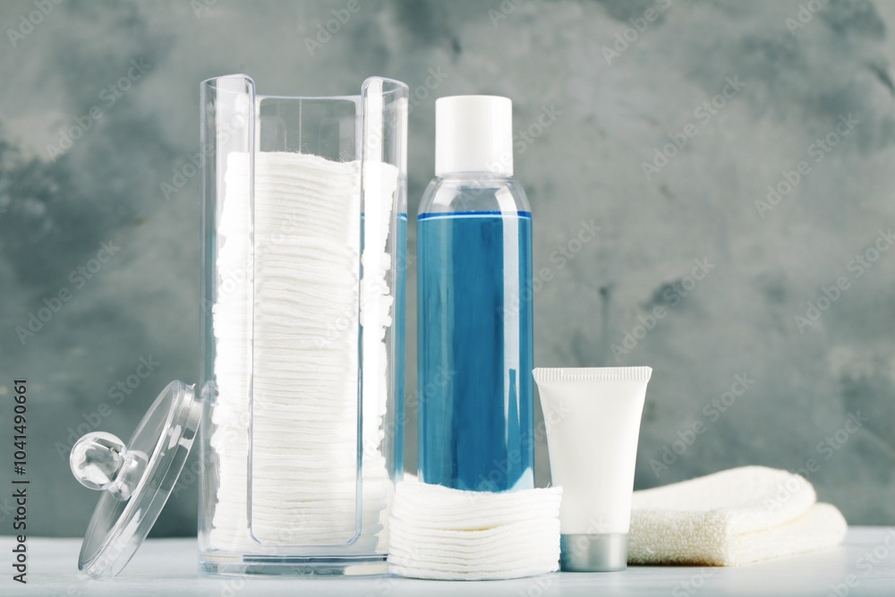Cotton pads in plastic jar and cosmetic bottles on gray background