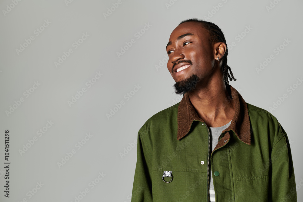 A young African American man showcases his fashion sense in stylish green attire against a sleek grey backdrop. A young African American man showcases his fashion sense in stylish green attire against a sleek grey backdrop.