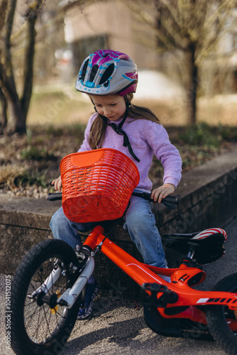  A 5-year-old girl rides her bike in a park, smiling and enjoying the sunny, green surroundings