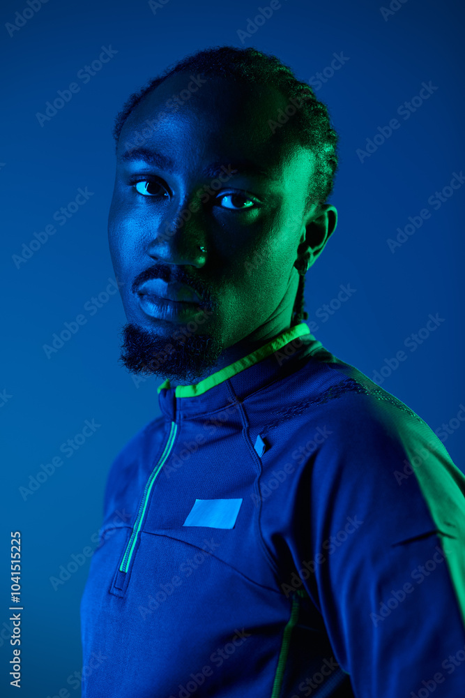 A young man showcases his fashion sense in a trendy outfit, illuminated by striking neon hues in a studio.