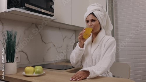 Apple proximity, Morning nutrition, Apple presence. In morning, woman savors refreshing glass of orange juice in kitchen, apples accompanying her as she practices healthy eating and vegan lifestyle.