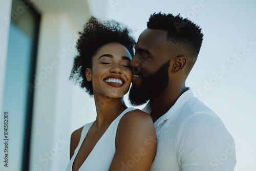 Happy young Black couple laughing while watching a movie at home on a sofa, with the focus on the woman joyfully closing her eyes as the man kisses her neck. This intimate and heartwarming moment capt photo